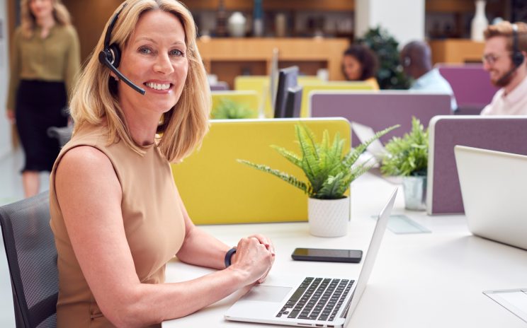 Portrait Of Mature Businesswoman Wearing Phone Headset Talking To Caller In Customer Services Centre